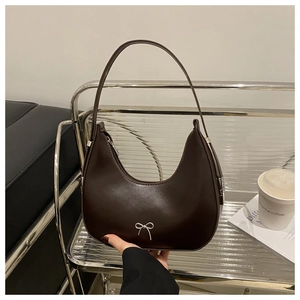 Detail of a brown hobo bag with a silver bow ornament on a stylish indoor shelf