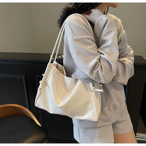 Side view of a creamy white glossy leather tote bag styled with a grey knit outfit