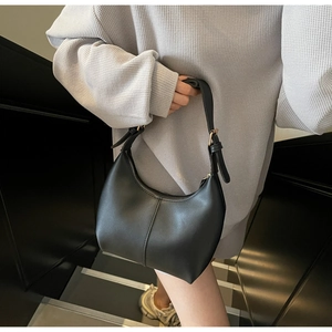 Detail of a minimalist black leather half-moon shoulder bag with adjustable gold buckle strap