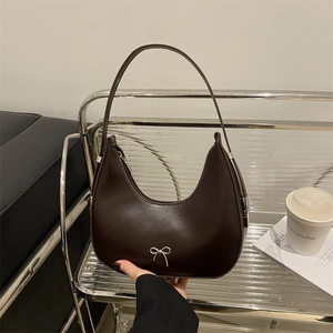 Dark brown faux leather hobo bag with a silver metal bow on a modern steel shelf