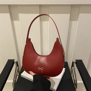 Chic red faux leather hobo bag with a silver bow on a minimalist chair setting