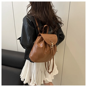 Rear view of model wearing a stylish brown leather backpack with gold buckle and black jacket