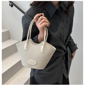 Detail of cream woven bucket bag showing trapezoid shape and leather handle in soft lighting