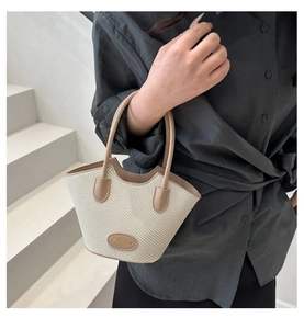 Chic woven bucket bag detail with khaki leather handles held by a model in casual attire