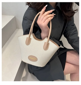 Close-up of beige woven bucket bag with brown leather handles and fashion logo patch
