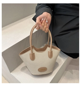 Detail of beige straw bucket bag with brown leather handles and wave opening