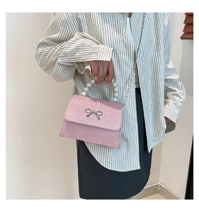 Pink sequin crossbody bag with pearl handle and metal bow detail shown on a model