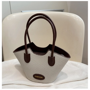 Close-up of woven bucket tote with brown leather handles and gold Fashion emblem