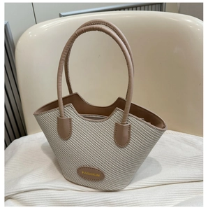 Detail of woven beige tote bag with brown leather trim and stylish fashion logo plate