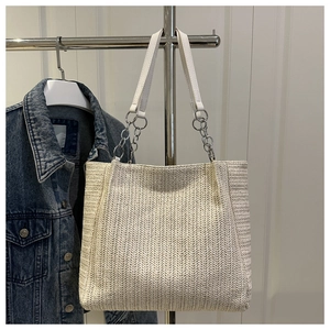 Detail of woven straw tote bag with silver chain strap and white leather texture