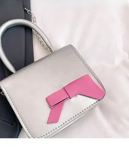 Detail of a silver mini square handbag with a prominent pink leather bow and metal chain