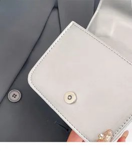 Close-up of silver leather handbag flap with magnetic snap button and precision stitching