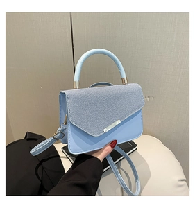 Detail of light blue PU leather shoulder bag with woven texture flap and gold hardware