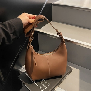 Minimalist brown underarm bag with wide strap and vertical stitching on a book