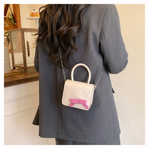 Detail of a beige mini shoulder bag with a pink bow and chain strap on a model