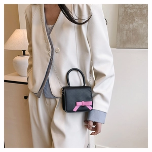 Detail of girls mini black leather crossbody bag with pink bow and silver chain strap