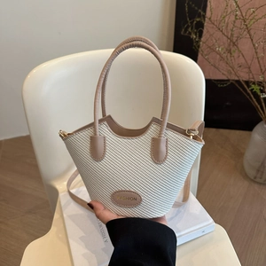 Beige woven bucket bag with wave design and leather handle on a white chair