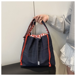 Detail of drawstring tote bag in navy denim with red checkered lining and fashion label