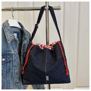 Detail of blue denim tote bag featuring red drawstring and plaid cotton lining interior