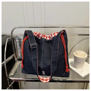 Detail view of the deep blue denim tote bag with red drawstring and plaid lining detail