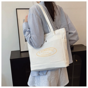 Detailed back view of a white canvas tote bag worn by a model in a minimalist room