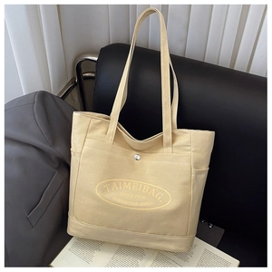 Detail of beige canvas tote bag with front pocket and elegant brand printing