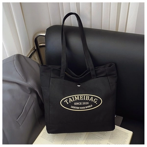 Detail of black canvas tote bag showing front pocket with silver buckle and brand patch