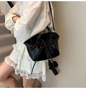 Detail of black drawstring cloud bag with ruffled edge and bow on a white dress model