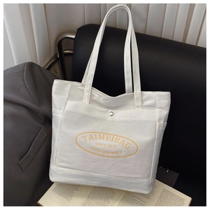 Detail of a white canvas tote bag with metal snap button pocket on a black sofa