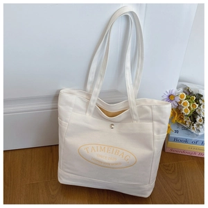 Close-up of white canvas tote bag with yellow oval print and silver metal buckle