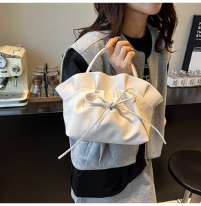 Detailed view of beige pleated handbag featuring a delicate ribbon bow and top handle
