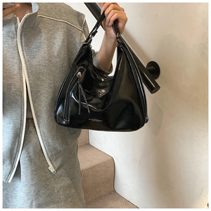 Détail du sac en cuir verni noir avec surpiqûres contrastées et plaque triangulaire