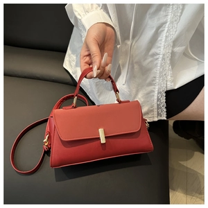 Detail of red leather crossbody bag with golden rectangular clasp and top handle