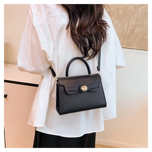 Close-up of black matte Kelly bag with gold twist lock and bow detail on white shirt