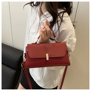 Detail of brick red leather crossbody square bag with gold hardware on a model