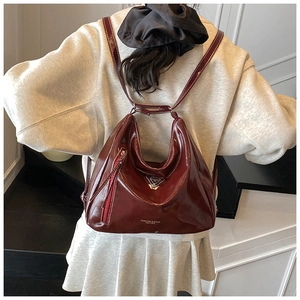 Détail d'un sac à dos en cuir verni bordeaux brillant avec logo triangulaire et fines bretelles