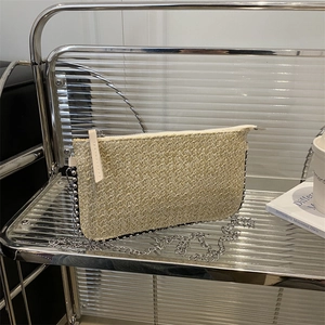 Sac bandoulière en paille tressée beige avec chaîne en métal argenté sur étagère