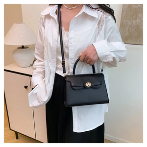 Close-up of black leather Kelly bag with golden twist lock and adjustable shoulder strap