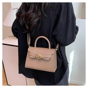 Woman carrying a chic khaki top handle bag with gold hardware clasp and shoulder strap