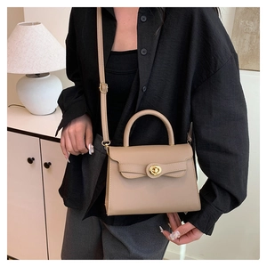 Detail of a beige trapezoid crossbody bag with gold-tone hardware on a female model