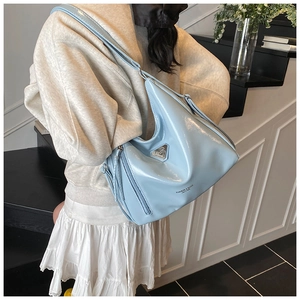 Détail du sac hobo bleu clair brillant avec logo métallique triangulaire sur l'avant