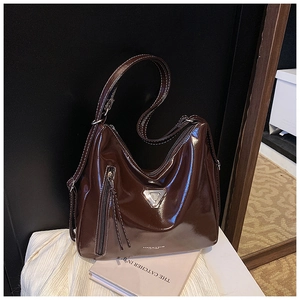 Détail d'un cabas en cuir verni marron foncé avec surpiqûres blanches et logo triangulaire