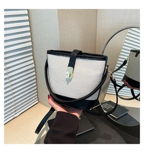 Détail du sac seau contrasté avec corps en paille tissée, finitions cuir noir et fermoir doré