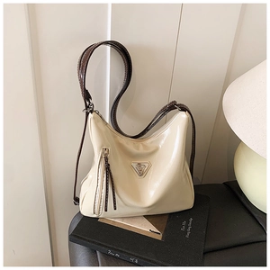 Détail du sac à main en cuir verni blanc crème avec logo triangulaire posé sur un livre
