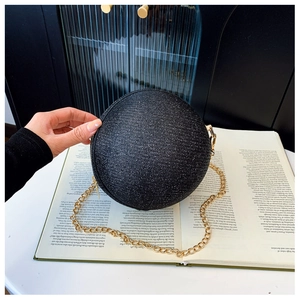 Detail of a spherical black sequin evening bag with a thin gold chain strap held by hand