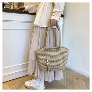 Detail of woven tote bag featuring a beige cotton rope texture and tassel bead ornament