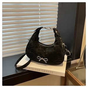 Detail of a black crescent hobo bag featuring silver bow accent and crinkled texture
