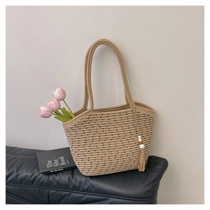Detail of woven straw tote bag with black dot texture, tassel charm and pink tulips
