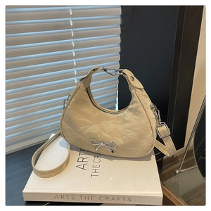 Macro shot of beige crescent tote bag with crinkled texture and silver bow charm