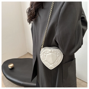 Detailopname van een witte gewatteerde hartvormige crossbodytas met gouden kettingriem